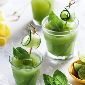 Three glasses of a green drink called aguafresca garnished with basil leaves and cucumber