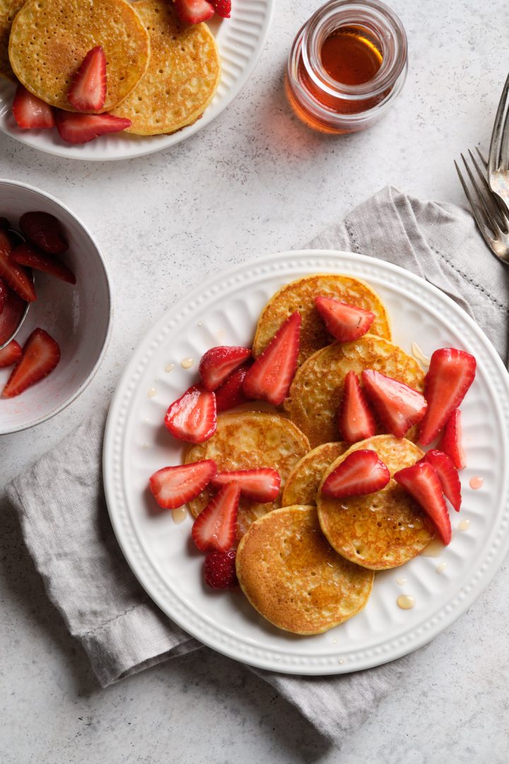 Gluten free cornmeal pancakes on a plate, served with strawberries, and maple syrup on the side