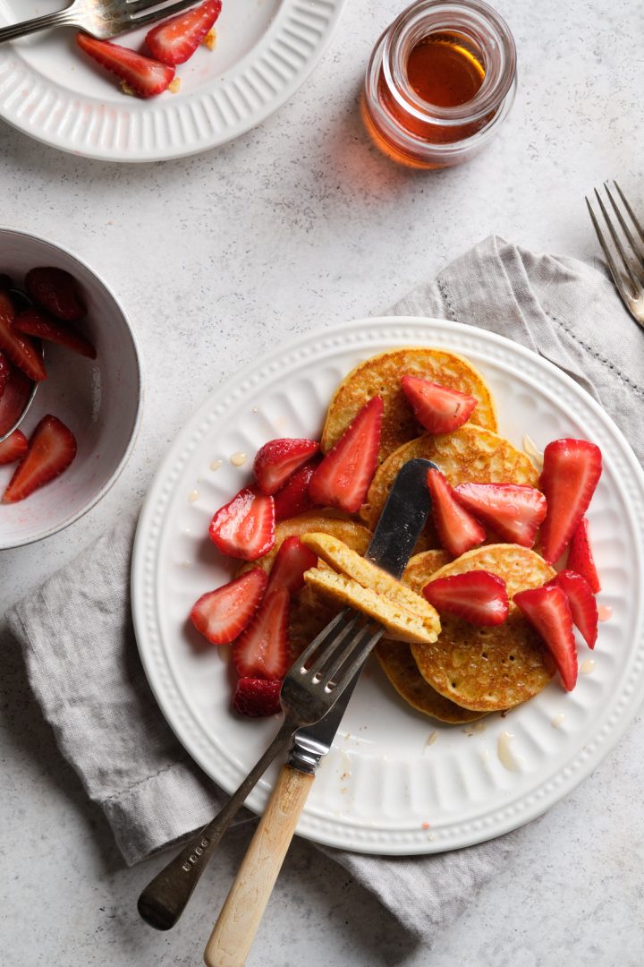Gluten free cornmeal pancakes on a plate, served with strawberries, and maple syrup on the side
