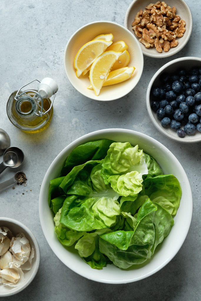 Ingredients for butter lettuce salad: butter lettuce leaves, blueberries, walnuts, lemon zest and juice, garlic and olive oil