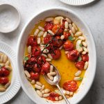 Roasted cherry tomatoes with white beans and two plates with servings of the tomato and bean dish