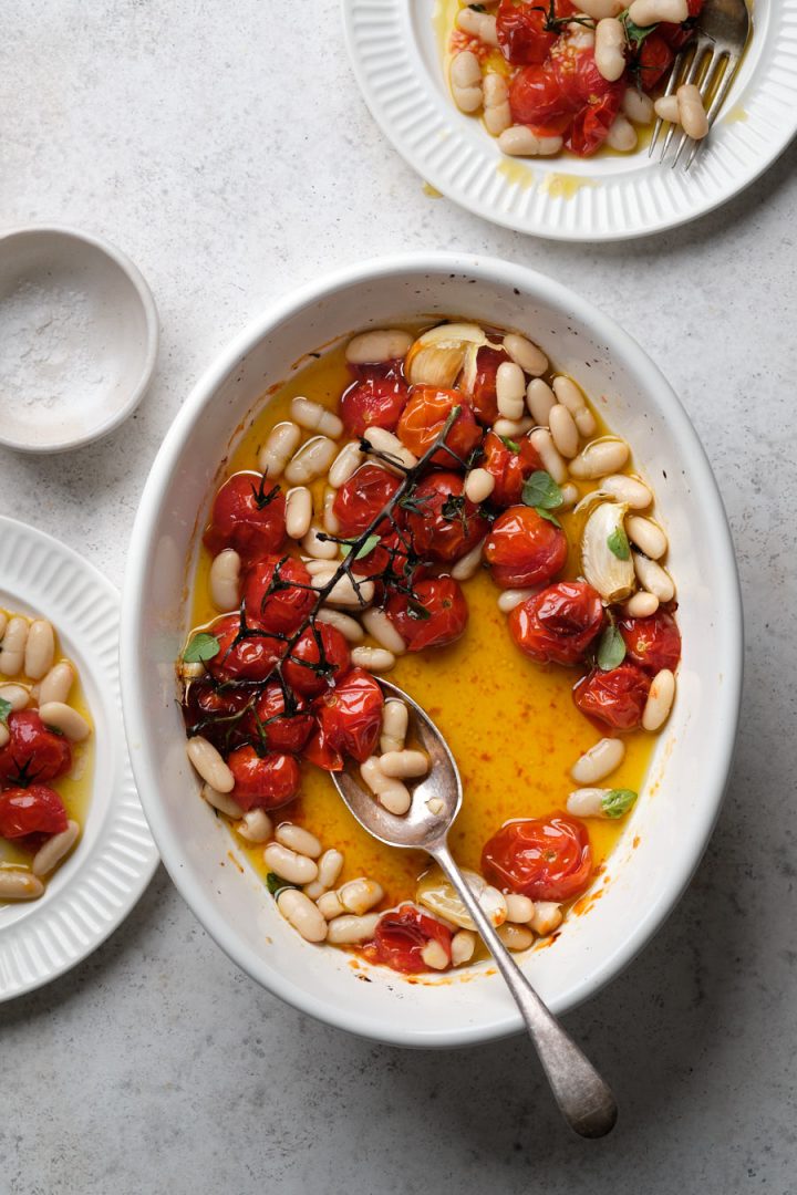 Roasted cherry tomatoes with white beans and two plates with servings of the tomato and bean dish