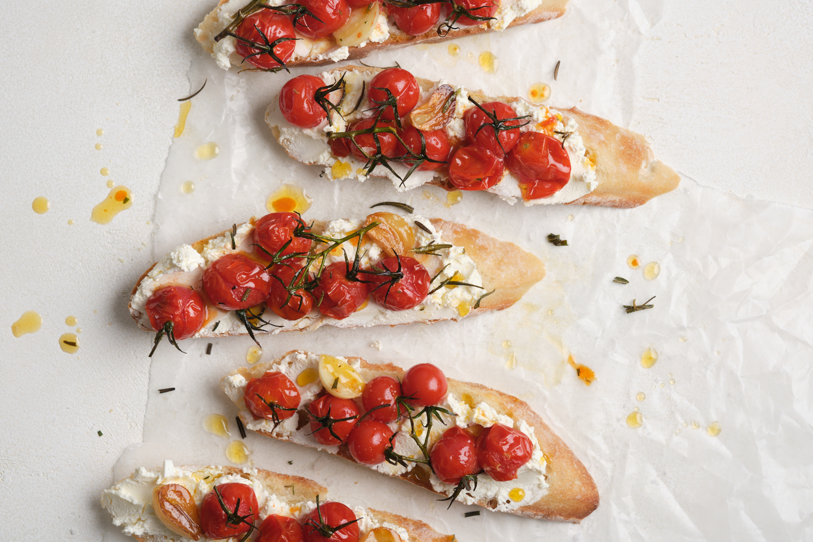 Slices of baguette spread with soft cheese and topped with roasted cherry tomatoes