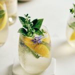A Lillet Blanc and elderflower liqueur cocktail in a glass garnished with lemon wedges and herbs