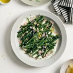 A plate of green beans with whipped feta with small dish of olive oil and lemons